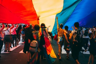 A group of people walking down the street underneath a giant Pride flag