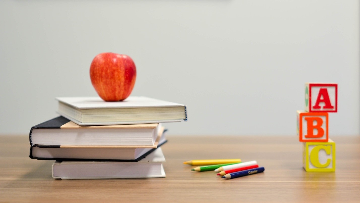 a stack of books, an apple on top, blocks and colored pencils on a desk