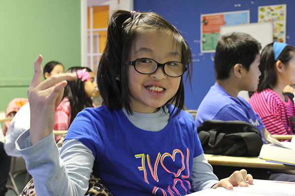 A student wearing glasses and a blue shirt sitting at her desk in a classroom