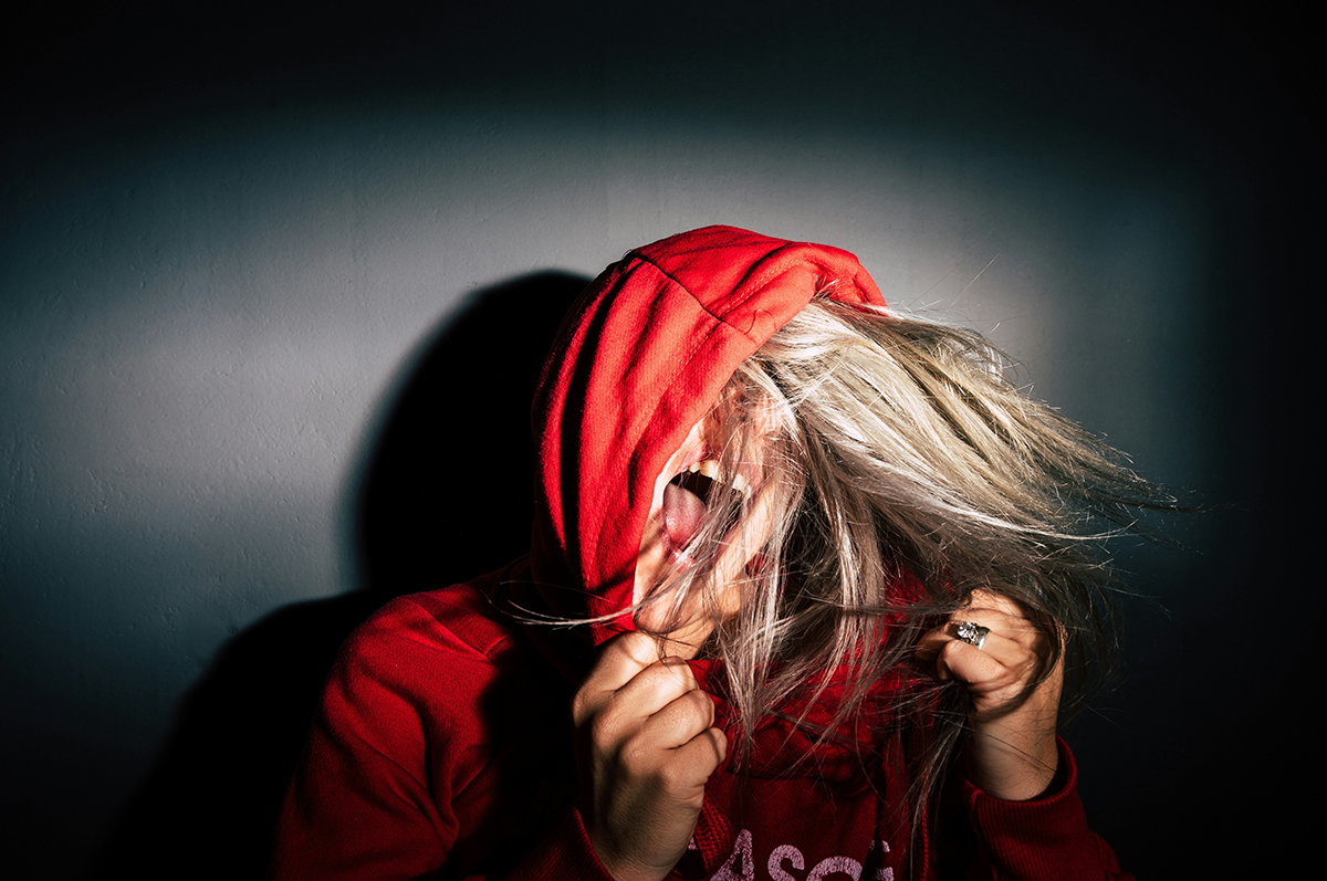 A woman with blonde hair screaming with a red hoodie pulled over her eyes