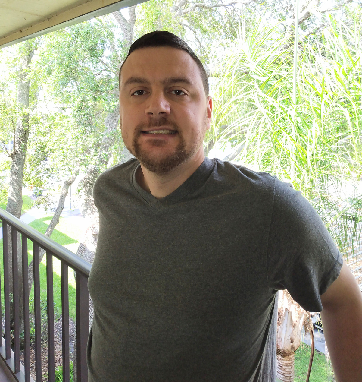 Ian H. wearing a grey shirt standing on a balcony