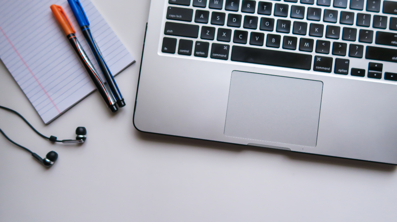 laptop keyboard with a notepad and pens next to it and a pair of headphones