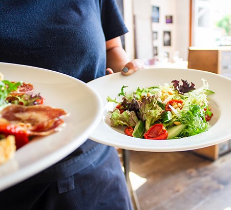 Restaurant server bringing two salads to a table