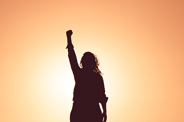 the silhouette of a person standing confidently with their arm above their head