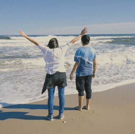 two people standing on the beach looking at the ocean