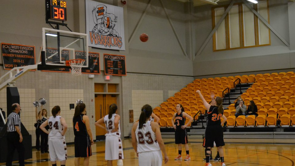 women's basketball game in a gym with orange seats