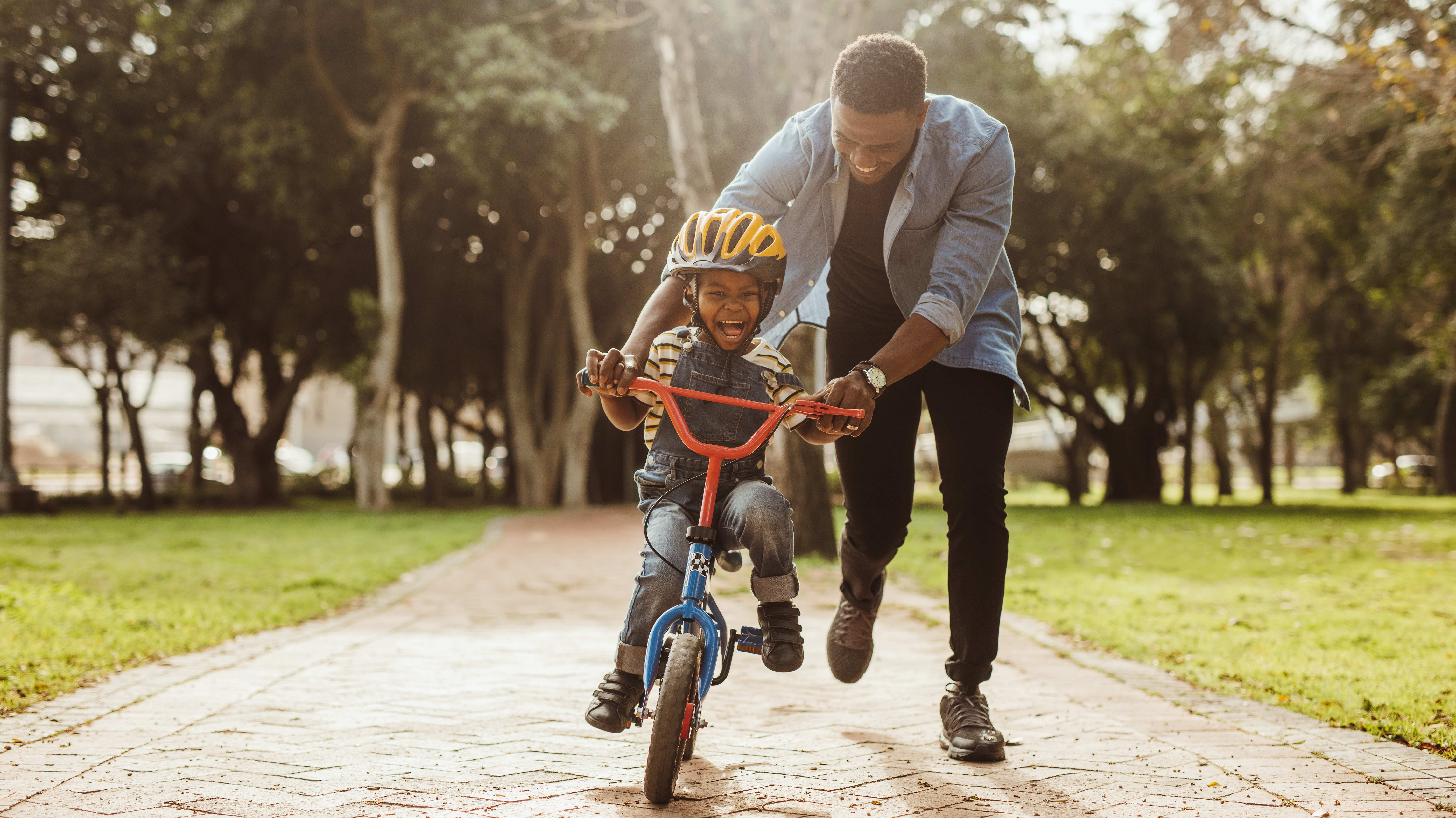 A man teaches his young son how to ride a bicycle on a sunny day in a public park 