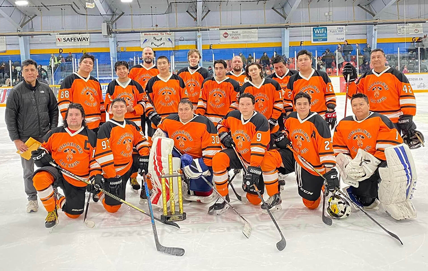 A hockey team in orange jerseys poses on the arena ice.