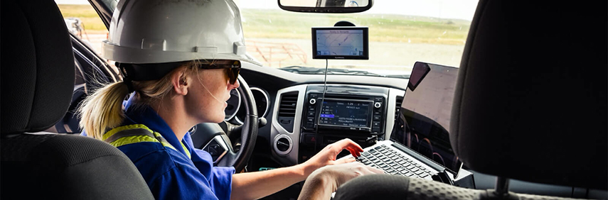 Assise derrière le volant d’un véhicule, une jeune chercheuse coiffée d’un casque de protection tape sur un ordinateur portable.