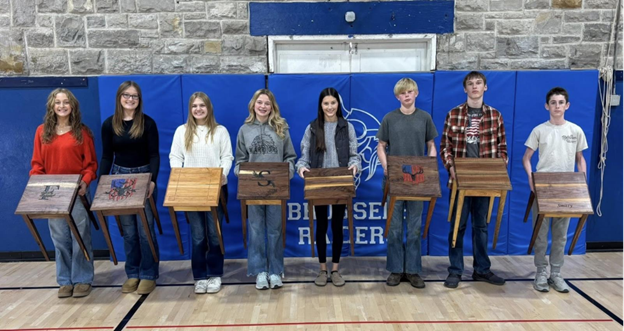 Group of students holding wooden tables. 