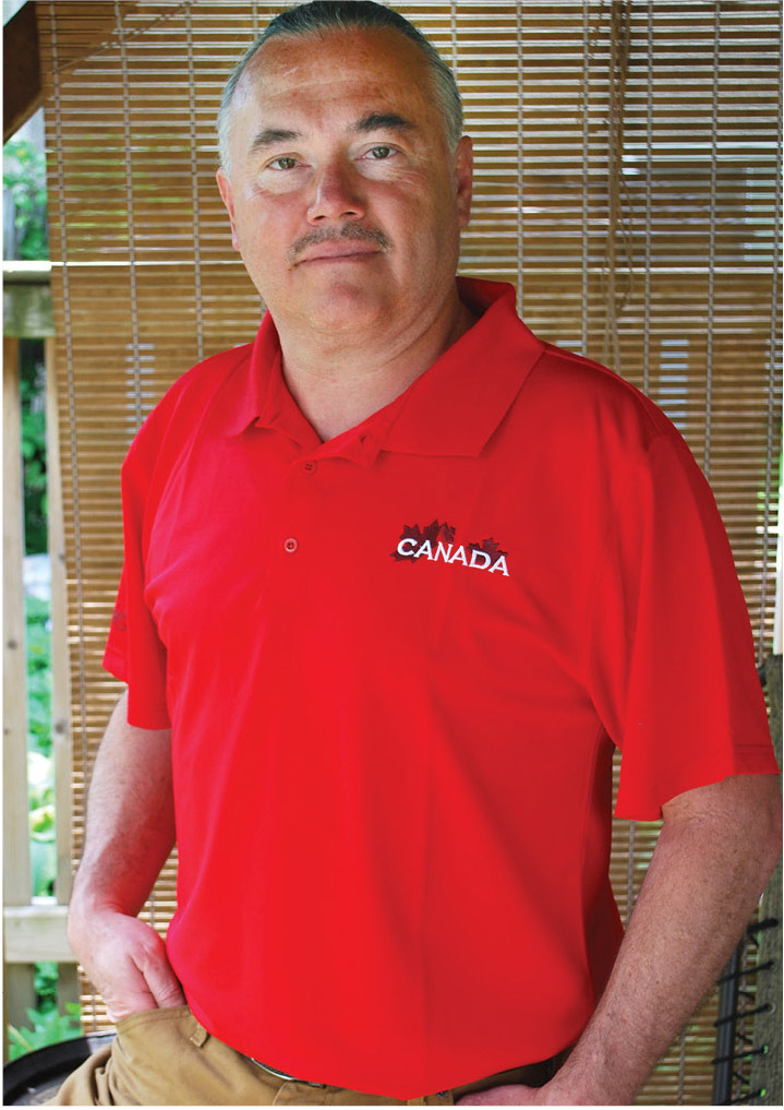 A man wears a vibrant red golf shirt with Canada on the upper left chest. There are small maple leaves behind the word Canada.