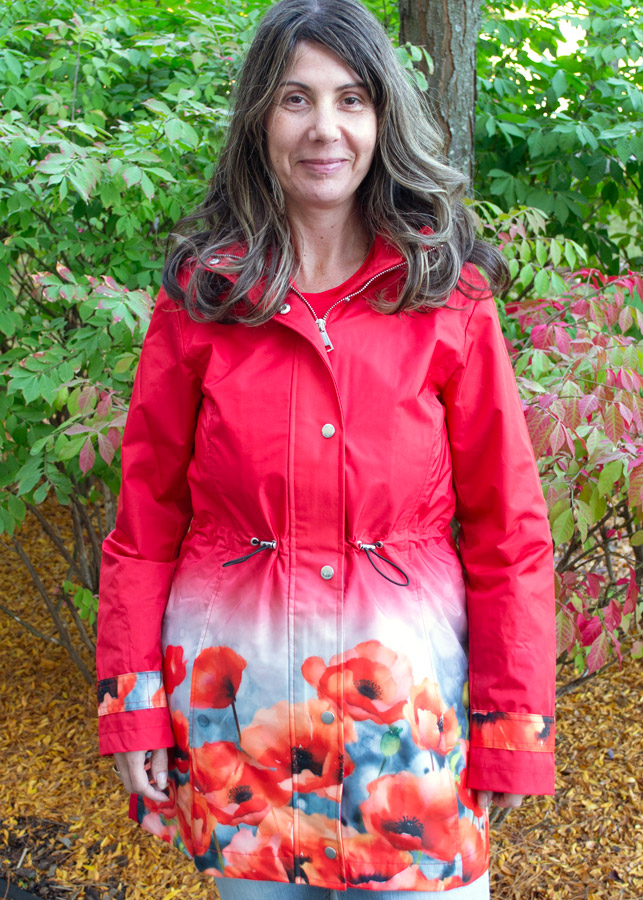 A woman wears a raincoat in a vibrant red color with bold poppy detailing at the hem and cuffs